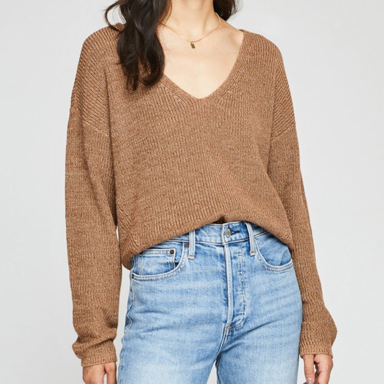 Woman waring a relaxed v neck sweater in caramel color with jeans.